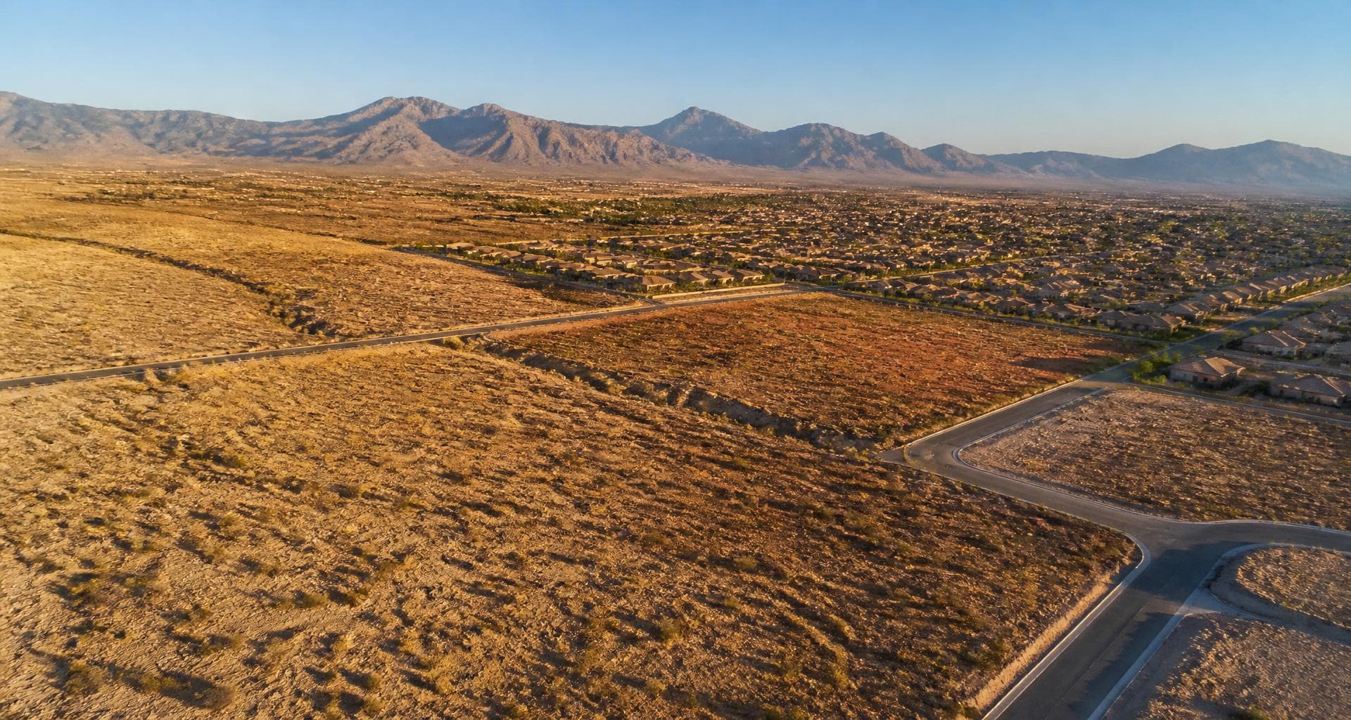 Aerial view of desert land at the edge of a Las Vegas residential subdivision with mountains on the horizon